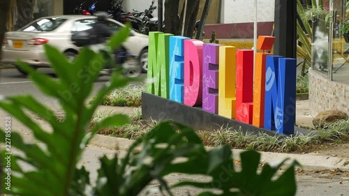 Colorful art sign at street in El Poblado district in Medellin Colombia with traffic and green leaves