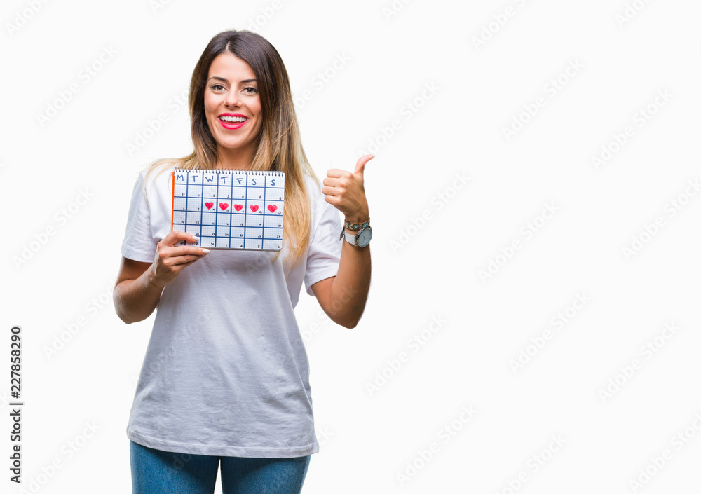 Young beautiful woman holding menstruation calendar over isolated background pointing and showing with thumb up to the side with happy face smiling Young beautiful woman holding menstruation calendar over isolated background pointing and showing with thumb up to the side with happy face smiling
