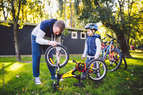 Father's day Caucasian dad and 5 year old son in the backyard near the house on the green grass on the lawn repairing a bicycle, pumping a bicycle wheel. Dad teaches how to repair a child's bike