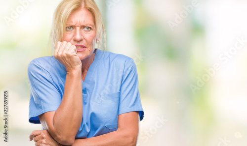 Middle age blonde woman wearing doctor nurse uniform over isolated background looking stressed and nervous with hands on mouth biting nails. Anxiety problem.