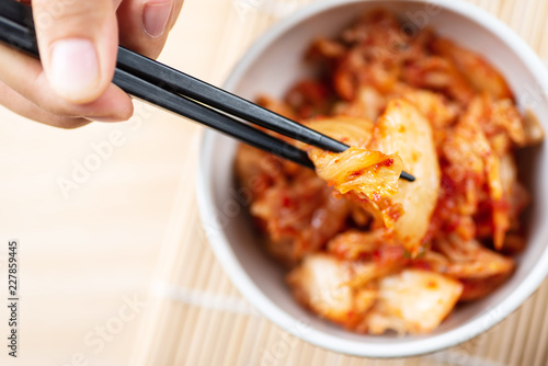 Hand holding chopsticks for eating kimchi cabbage in a bowl, Korean food