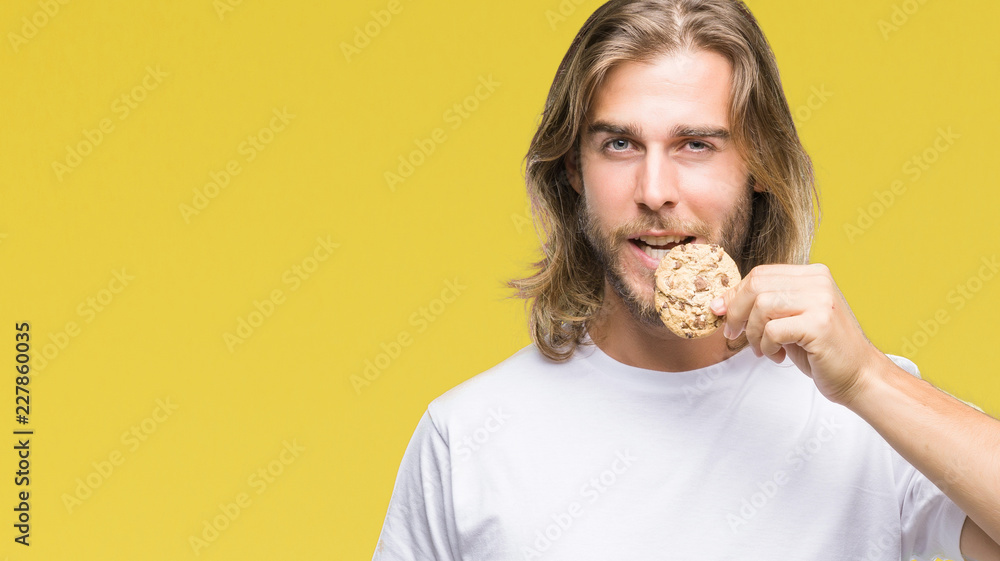 Young handsome man with long hair eating chocolate cooky over isolated background with a confident expression on smart face thinking serious Young handsome man with long hair eating chocolate cooky over isolated background with a confident expression on smart face thinking serious
