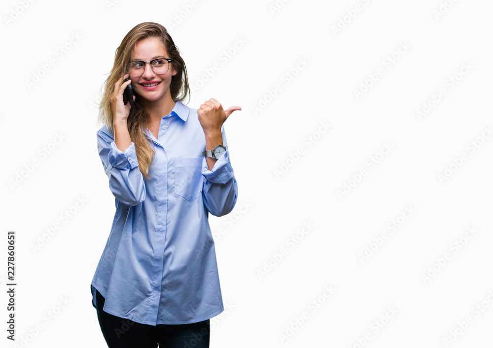 Young beautiful blonde business woman calling using smartphone over isolated background pointing and showing with thumb up to the side with happy face smiling Young beautiful blonde business woman calling using smartphone over isolated background pointing and showing with thumb up to the side with happy face smiling