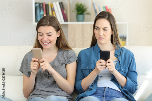 Envious woman looking at her friend texting in a phone photo