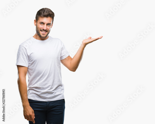 Young handsome man over isolated background smiling cheerful presenting and pointing with palm of hand looking at the camera. © Krakenimages.com
