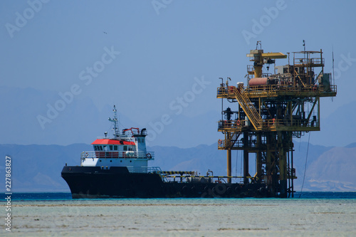 Oil production rig in the sea, landscape. Red Sea, Egypt, Africa, Uninhabited islands. Industrial view, nature operations, blue water and maintenance ships around. Modern technologies