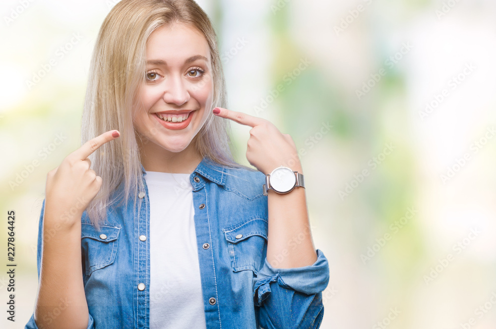 Young blonde woman over isolated background smiling confident showing and pointing with fingers teeth and mouth. Health concept. Young blonde woman over isolated background smiling confident showing and pointing with fingers teeth and mouth. Health concept.
