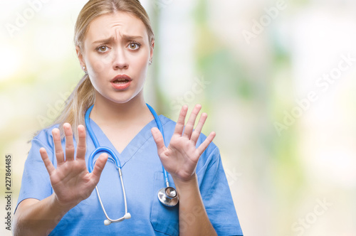 Fototapeta kuchenna Young blonde surgeon doctor woman over isolated background afraid and terrified with fear expression stop gesture with hands, shouting in shock. Panic concept.