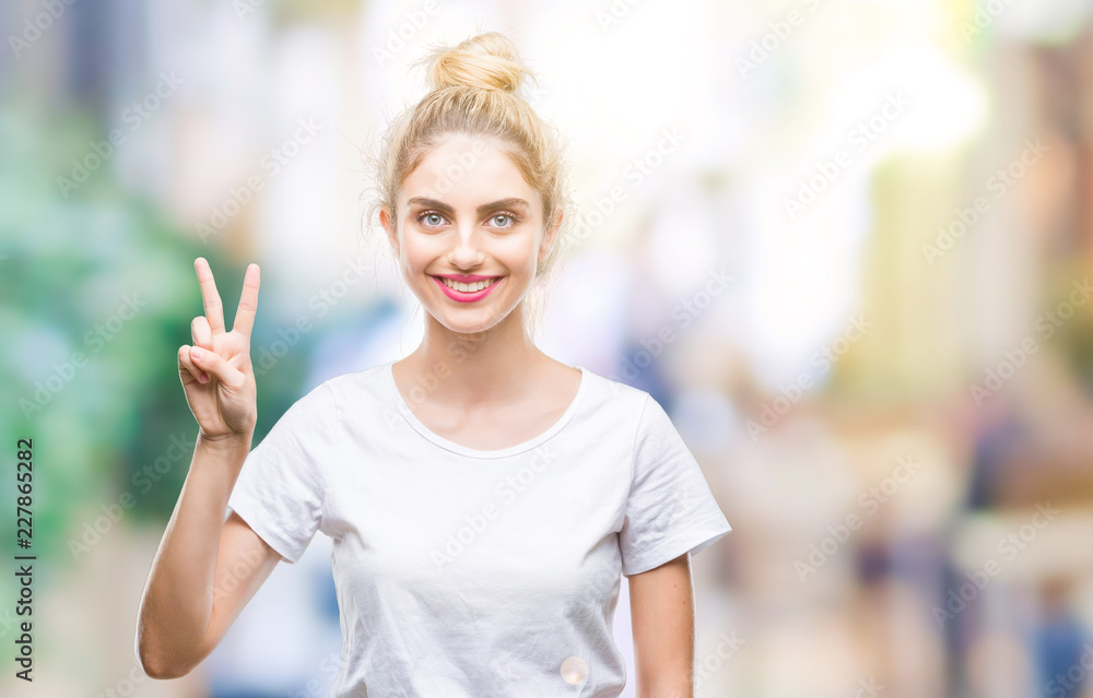 Fototapeta premium Young beautiful blonde woman wearing white t-shirt over isolated background showing and pointing up with fingers number two while smiling confident and happy.