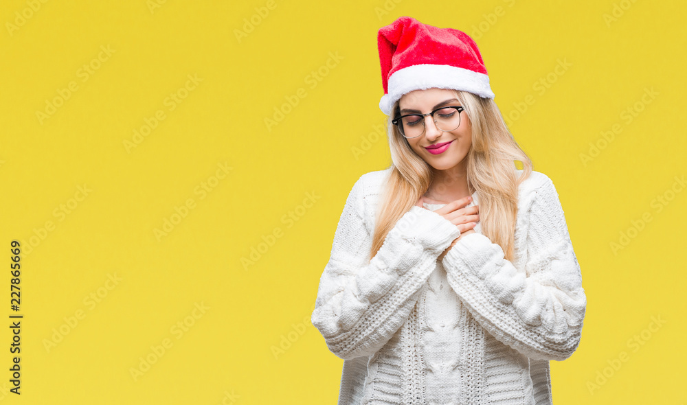 Young beautiful blonde woman wearing christmas hat over isolated background smiling with hands on chest with closed eyes and grateful gesture on face. Health concept. Young beautiful blonde woman wearing christmas hat over isolated background smiling with hands on chest with closed eyes and grateful gesture on face. Health concept.