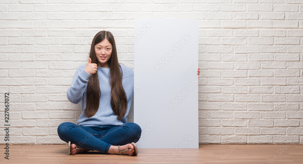 Young Chinese woman over brick wall holding banner happy with big smile doing ok sign, thumb up with fingers, excellent sign Young Chinese woman over brick wall holding banner happy with big smile doing ok sign, thumb up with fingers, excellent sign