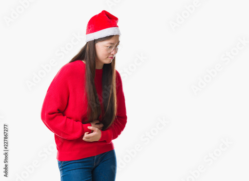 Young Chinese woman over isolated background wearing christmas hat with hand on stomach because nausea, painful disease feeling unwell. Ache concept.