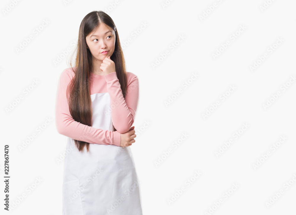 Young Chinese shop owner woman over isolated background wearing white apron serious face thinking about question, very confused idea Young Chinese shop owner woman over isolated background wearing white apron serious face thinking about question, very confused idea