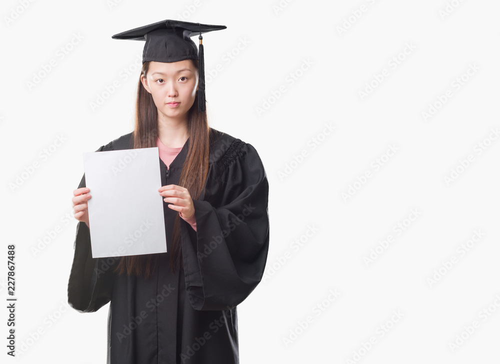 Young Chinese woman wearing graduate uniform holding paper degree with a confident expression on smart face thinking serious Young Chinese woman wearing graduate uniform holding paper degree with a confident expression on smart face thinking serious