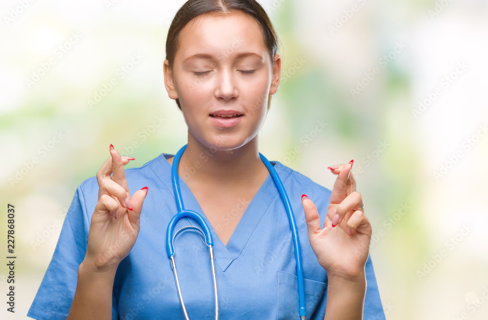 Young caucasian doctor woman wearing medical uniform over isolated background smiling crossing fingers with hope and eyes closed. Luck and superstitious concept. Young caucasian doctor woman wearing medical uniform over isolated background smiling crossing fingers with hope and eyes closed. Luck and superstitious concept.
