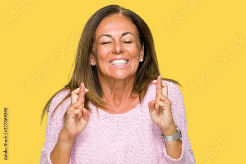 Beautiful middle age adult woman wearing winter sweater over isolated background smiling crossing fingers with hope and eyes closed. Luck and superstitious concept.