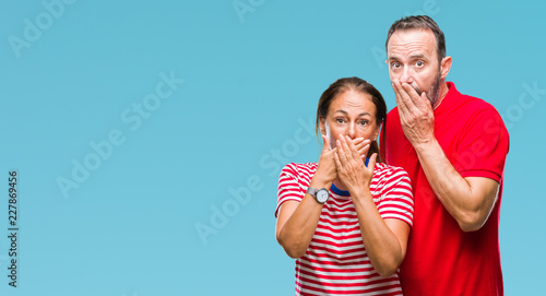 Middle age hispanic couple in love over isolated background shocked covering mouth with hands for mistake. Secret concept.