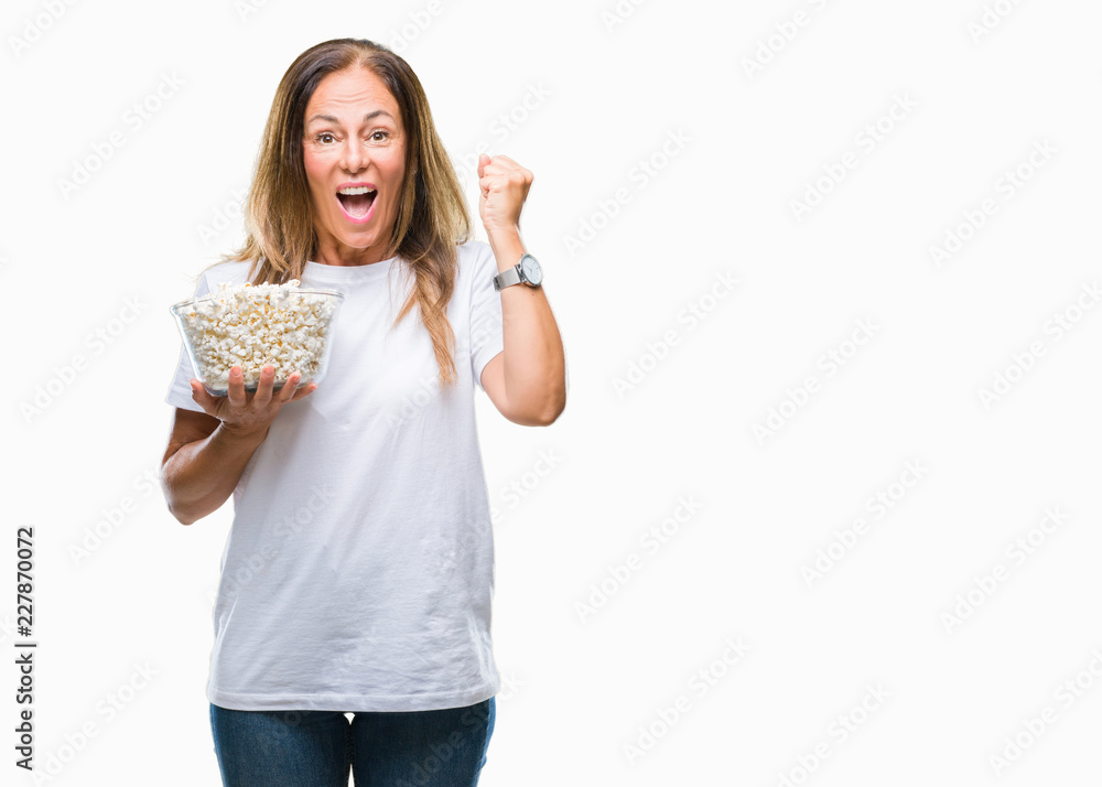 Middle age hispanic woman eating popcorn over isolated background screaming proud and celebrating victory and success very excited, cheering emotion Middle age hispanic woman eating popcorn over isolated background screaming proud and celebrating victory and success very excited, cheering emotion