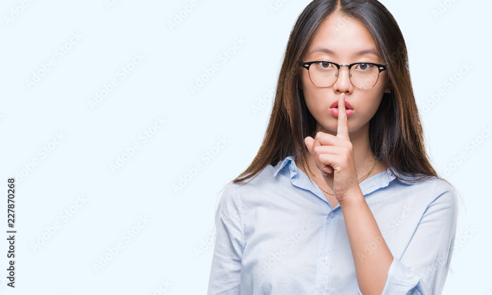 Young asian business woman wearing glasses over isolated background asking to be quiet with finger on lips. Silence and secret concept. Young asian business woman wearing glasses over isolated background asking to be quiet with finger on lips. Silence and secret concept.