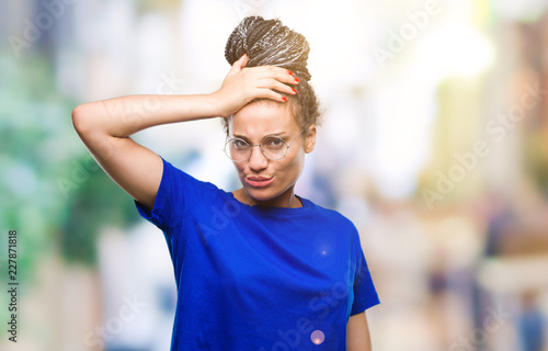 Young braided hair african american girl wearing glasses over isolated background confuse and wonder about question. Uncertain with doubt, thinking with hand on head. Pensive concept.