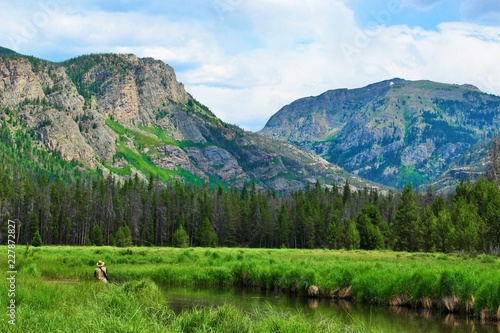 Rocky Mountain National Park lake in July with mountains in the background and a man fly fishing in the foreground