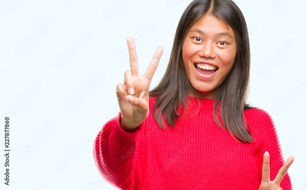 Young asian woman wearing winter sweater over isolated background smiling looking to the camera showing fingers doing victory sign. Number two. Young asian woman wearing winter sweater over isolated background smiling looking to the camera showing fingers doing victory sign. Number two.