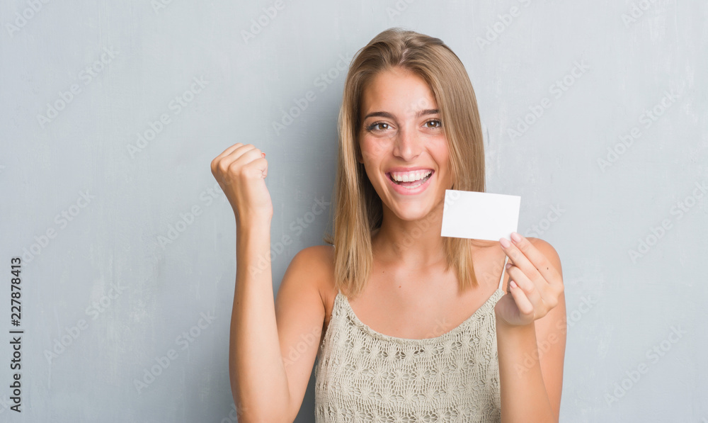 Beautiful young woman over grunge grey wall holding blank visit card screaming proud and celebrating victory and success very excited, cheering emotion Beautiful young woman over grunge grey wall holding blank visit card screaming proud and celebrating victory and success very excited, cheering emotion