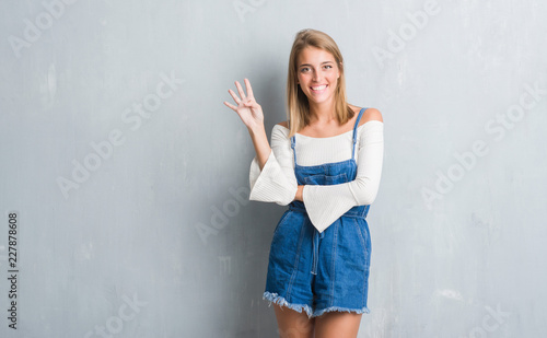 Beautiful young woman standing over grunge grey wall showing and pointing up with fingers number four while smiling confident and happy.