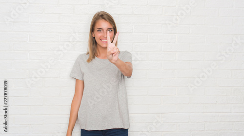 Beautiful young woman over white brick wall showing and pointing up with fingers number two while smiling confident and happy. © Krakenimages.com