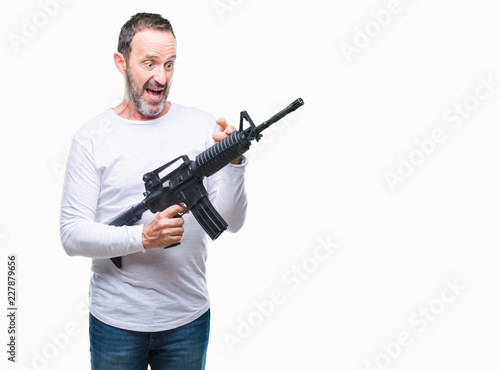Middle age senior hoary criminal man holding gun weapon over isolated background very happy pointing with hand and finger