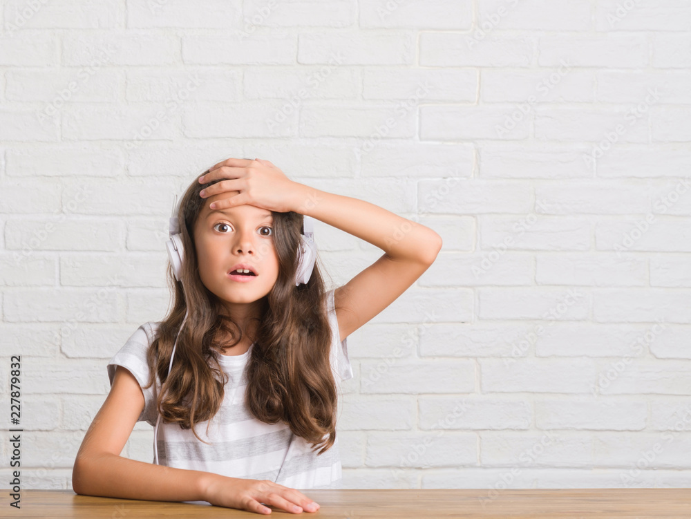 Young hispanic kid sitting on the table wearing headphones stressed with hand on head, shocked with shame and surprise face, angry and frustrated. Fear and upset for mistake. Young hispanic kid sitting on the table wearing headphones stressed with hand on head, shocked with shame and surprise face, angry and frustrated. Fear and upset for mistake.