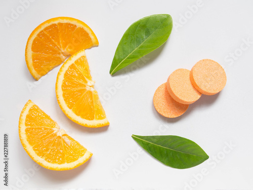 Top view of vitamin c effervescent tablets with fresh juicy orange fruit slice and green leaf on white table. Vitamins from foods or supplements choices. Health and medical concept. photo