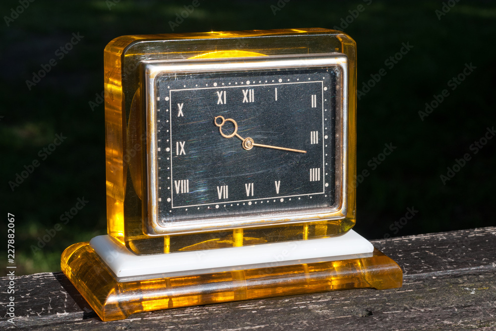 Old square amber desktop clock with a black dial, gold hands and a  transparent body on a black background on a brown wooden stand Stock-Foto |  Adobe Stock