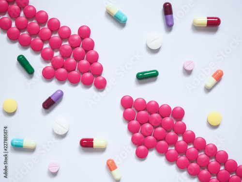 Fotografie Two pink arrows made by pills among many different medical tablets/capsules on blue tone background