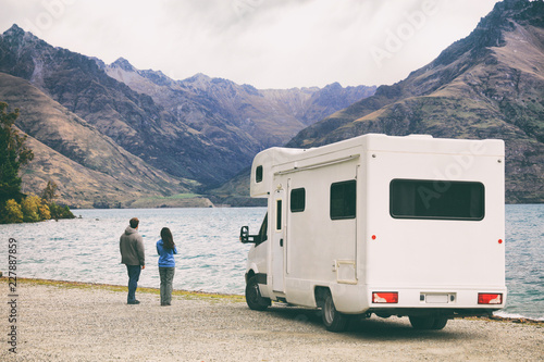RV motorhome camper van road trip young people on New Zealand travel vacation adventure, Two tourists looking at lake and mountains on pit stop next to their rental car.