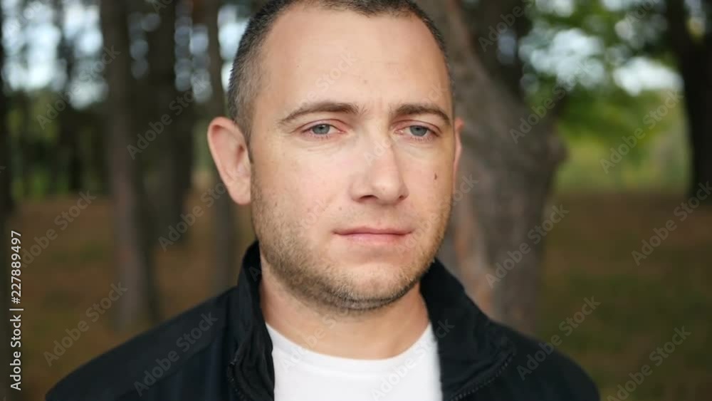 A man with a beard with a serious thoughtful look looks into the distance against the background of the park. Close-up of a man. Melenoe camera movement around. A man with a beard with a serious thoughtful look looks into the distance against the background of the park. Close-up of a man. Melenoe camera movement around.