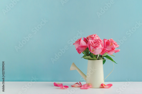 Withered rose flowers at watering can on white and blue wooden background