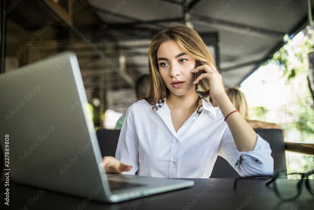Young pretty woman talking on the phone with a laptop on table in cafe Young pretty woman talking on the phone with a laptop on table in cafe