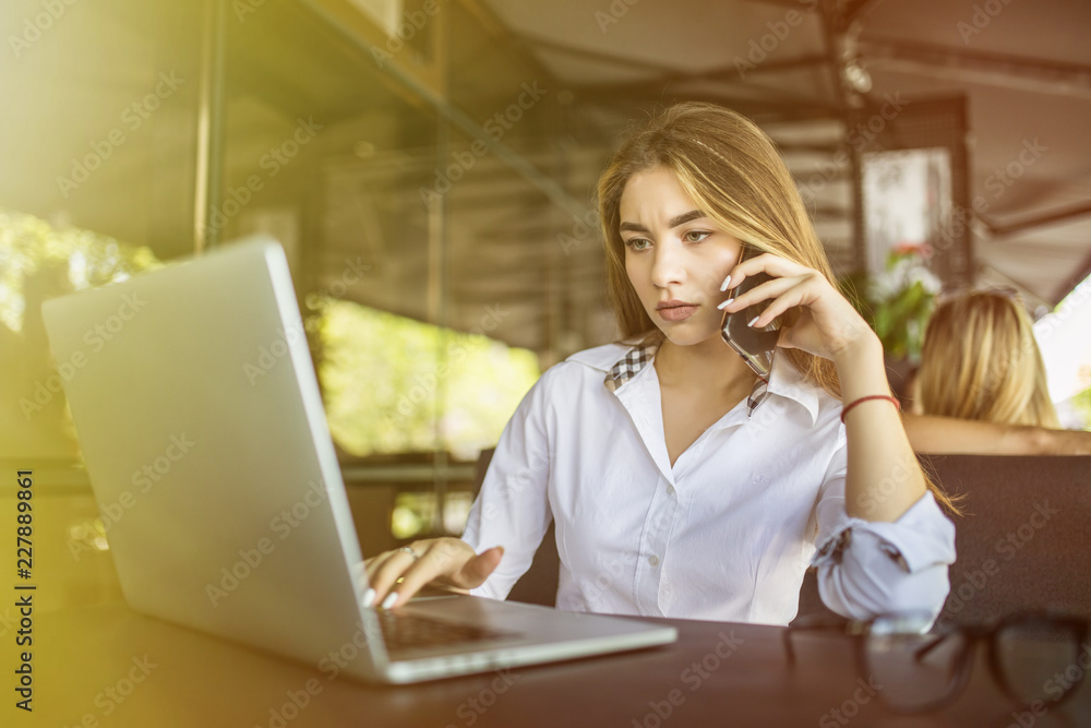 Young pretty woman talking on the phone with a laptop on table in cafe Young pretty woman talking on the phone with a laptop on table in cafe