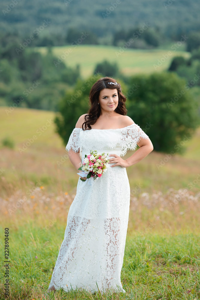Beautiful brunette girl with a bouquet of flowers. Young woman with long hair in a white lace dress. Summer female full-length portrait Beautiful brunette girl with a bouquet of flowers. Young woman with long hair in a white lace dress. Summer female full-length portrait