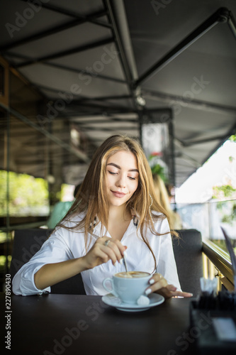 portrait of beautiful charming woman is stirring coffee in cafe and thinking
