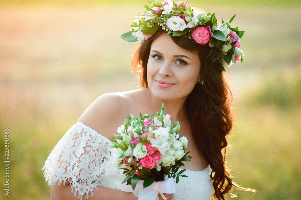 Beautiful brunette girl with a bouquet and a wreath of flowers. Young woman with long hair in a white lace dress. Summer female portrait Beautiful brunette girl with a bouquet and a wreath of flowers. Young woman with long hair in a white lace dress. Summer female portrait