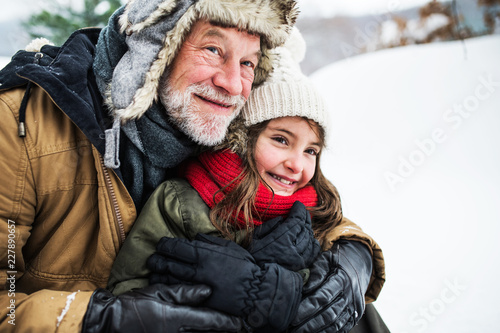 A portrait of senior grandfather and a small girl in snow on a winter day.