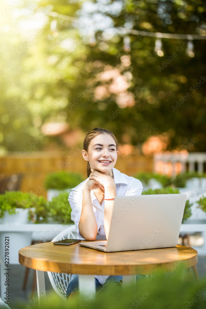 Young girl sitting at outdoor coffee shop using laptop. Young girl sitting at outdoor coffee shop using laptop.