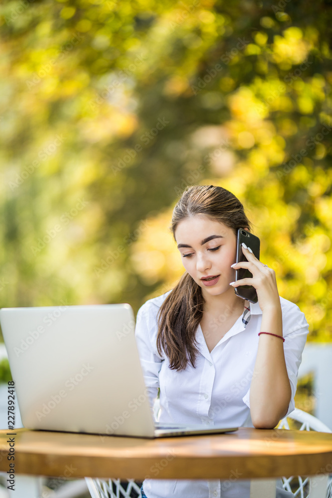 Happy businesswoman sitting at the table and talking on the phone in outdoors cafe. Looking away Happy businesswoman sitting at the table and talking on the phone in outdoors cafe. Looking away
