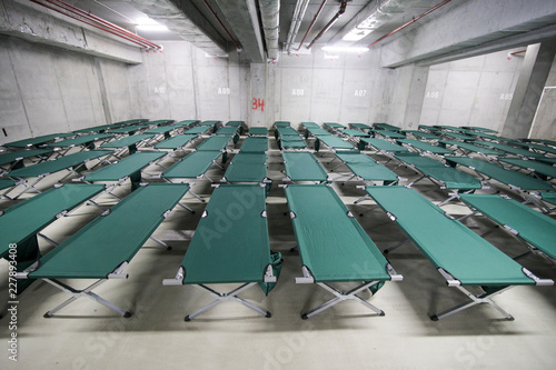 Camp folding cots are being set up in the underground parking of a stadium