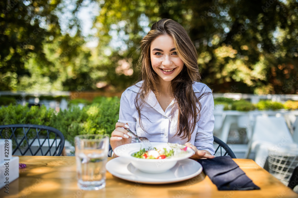 Young woman is eating mixed vegetable salad in cafe outdoors Young woman is eating mixed vegetable salad in cafe outdoors