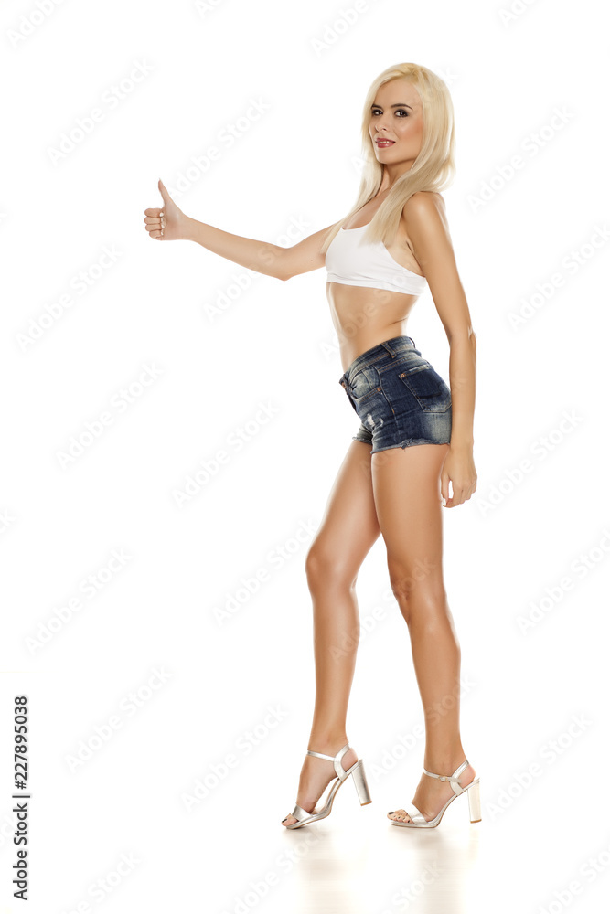 young pretty blonde woman posing in short jeans on white background and showing thumbs up young pretty blonde woman posing in short jeans on white background and showing thumbs up