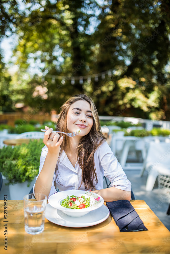 Young woman is eating mixed vegetable salad in cafe on terrace