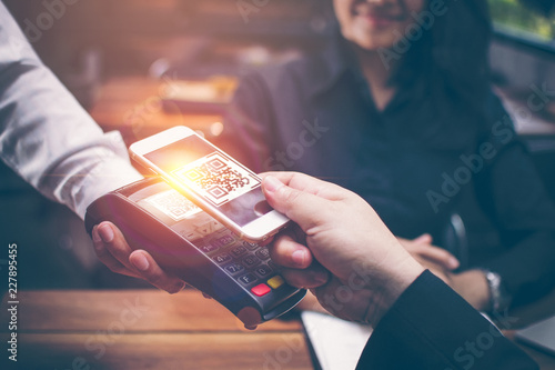 Young man hands are Smartphone to scan a QR CODE filing from a credit card reader to pay for food and beverages in restaurants which have a romantic atmosphere by the Asian girls are sitting together.